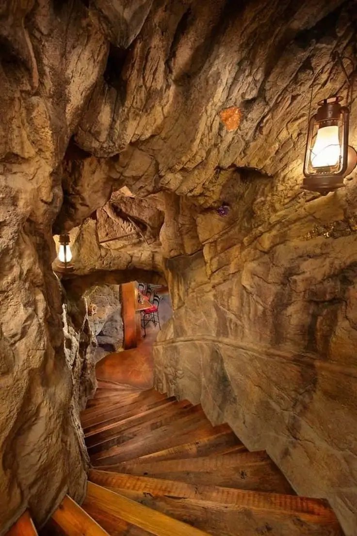 Escalier en bois intégré dans une grotte artificielle avec parois rocheuses sculptées et éclairages muraux, décor immersif style grotte