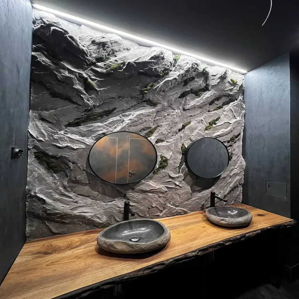 Salle de bain design avec mur en béton sculpté façon roche naturelle, vasques en pierre et éclairage indirect