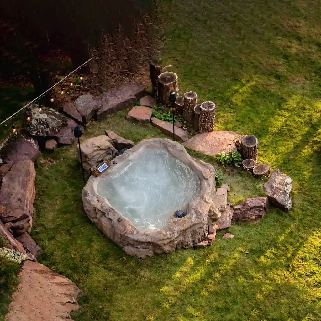 Jacuzzi extérieur en béton sculpté avec effet roche naturelle, décor végétal, éclairage et ambiance rustique – Réalisation Art Déco Béton