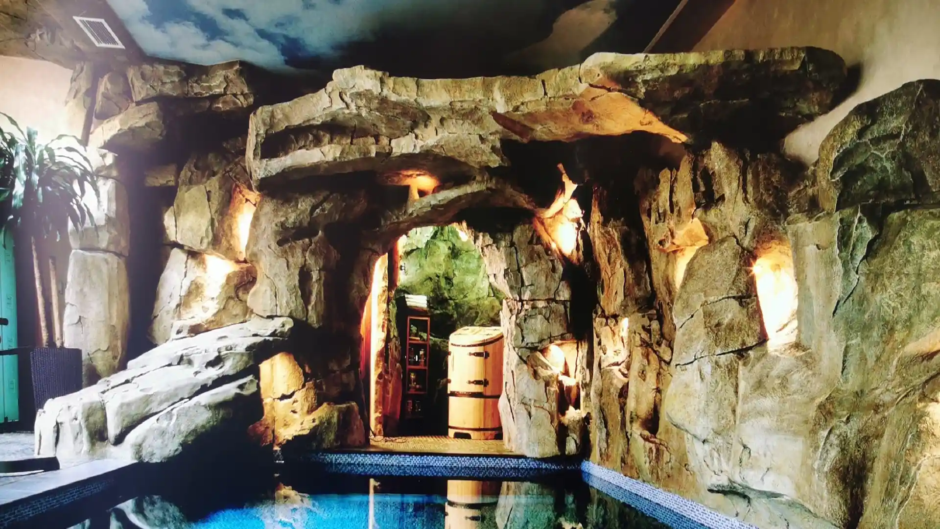 Piscine intérieure avec roches sculptées en béton, toboggan, mosaïque bleue et décor tropical – Réalisation Art Déco Béton