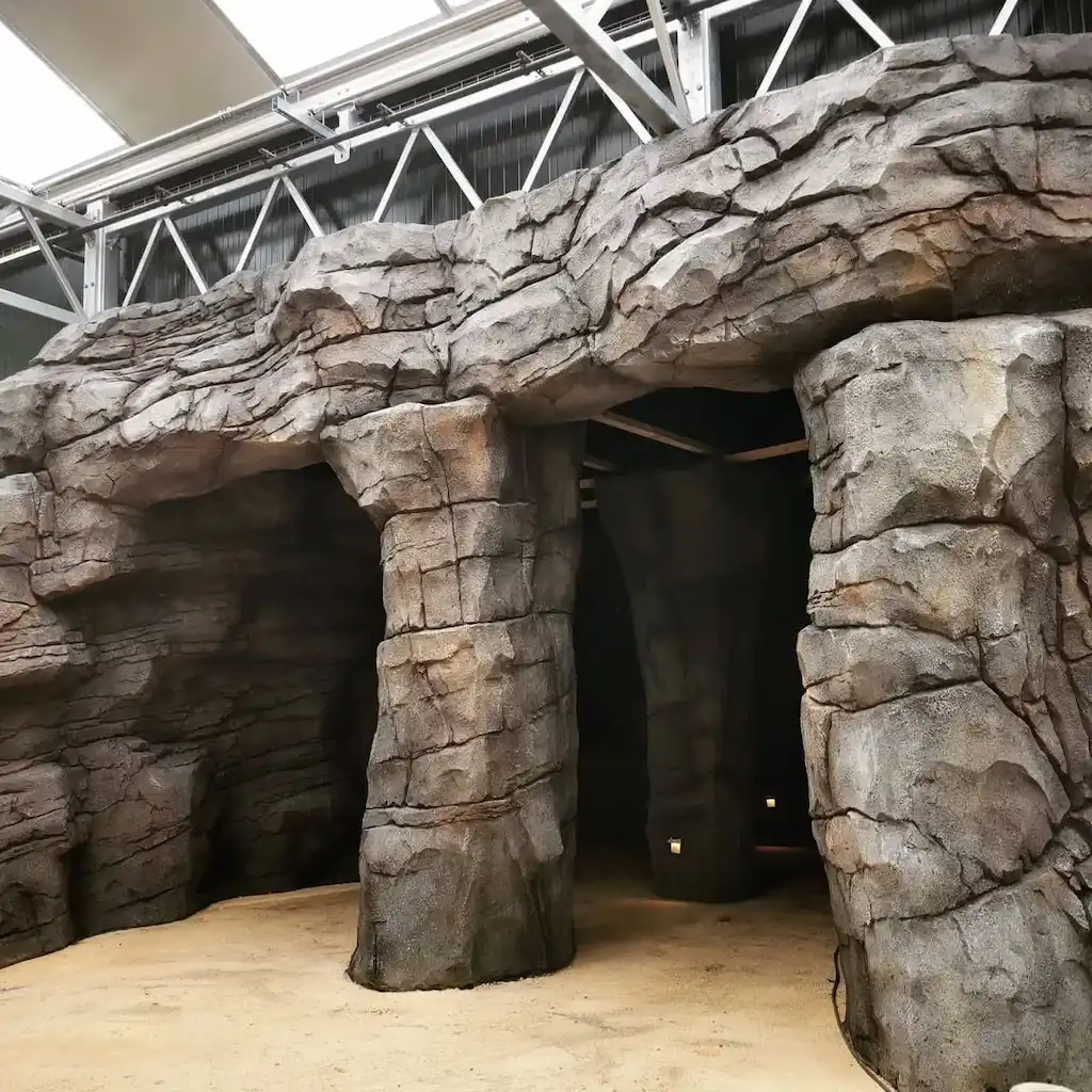 Structure extérieure façon grotte avec colonnes et arches en béton sculpté, sol sablonneux et cadre couvert – Réalisation Art Déco Béton