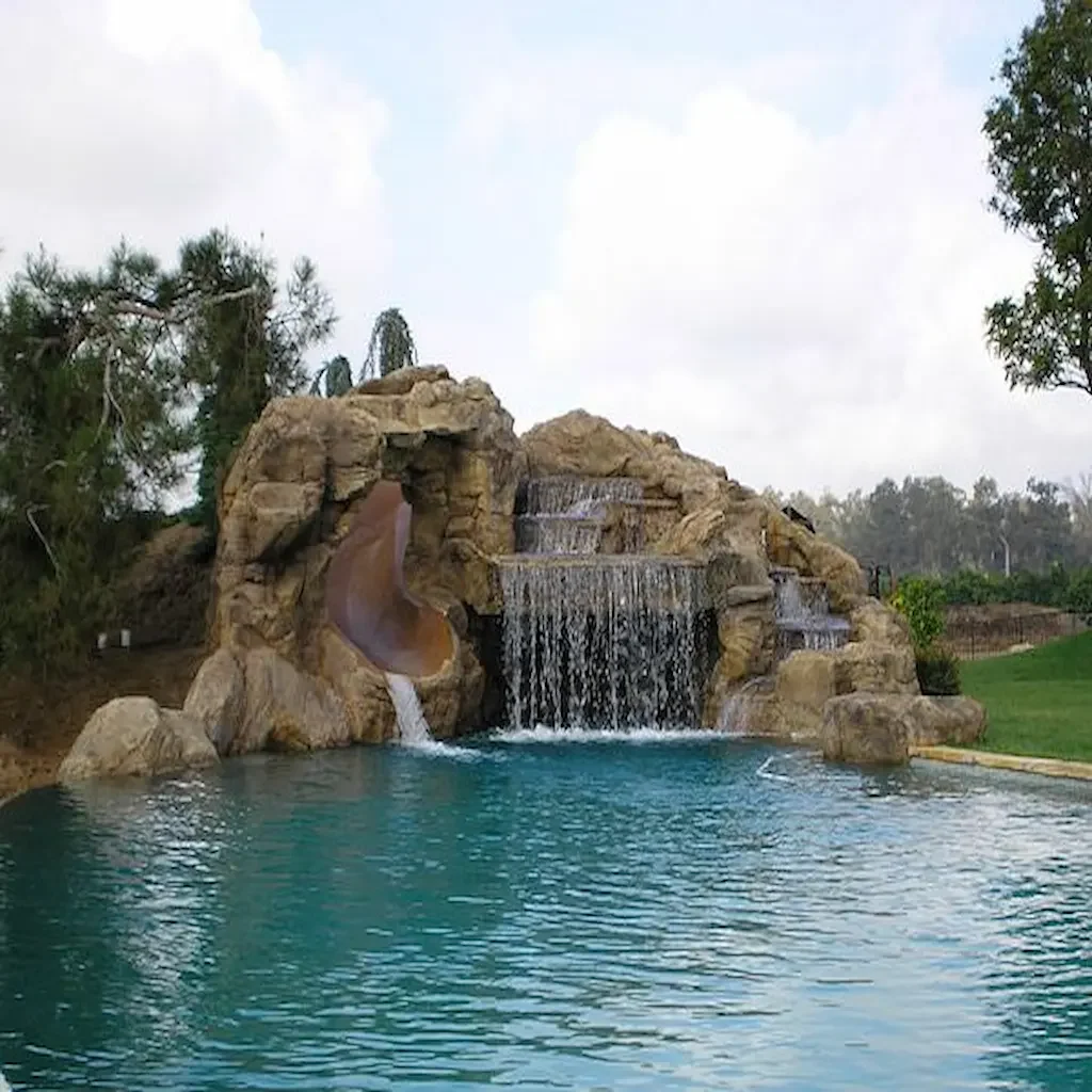 Piscine extérieure avec roches artificielles en béton, cascade décorative et toboggan sculpté – Réalisation Art Déco Béton
